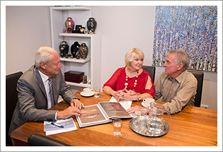 A funeral director and couple reviewing funeral arrangements at a consultation table, with display urns in the background