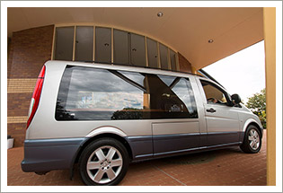 A silver Mercedes hearse parked under a covered porte-cochère