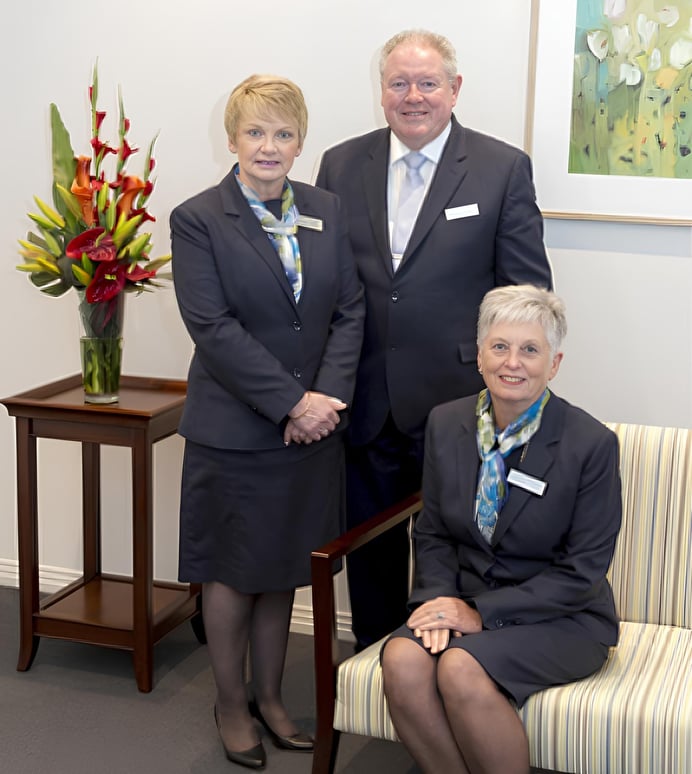 Three McGrath Funerals staff members in dark suits posing together in their office