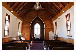Timber-vaulted interior of the chapel with wooden pews, a chandelier, and flowers at the altar