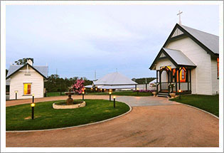 Wide view of the chapel grounds at dusk with multiple white heritage buildings and a circular garden