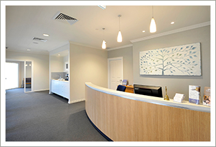 A curved timber reception desk in a bright waiting area with a tree-of-life artwork on the wall