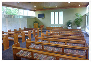Rows of timber pews inside a modern crematorium chapel with large windows